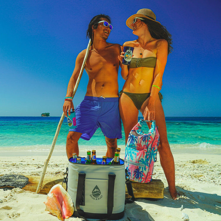 Man and women on the beach enjoying the sun and a drinks that are in their Skog å Kust soft cooler