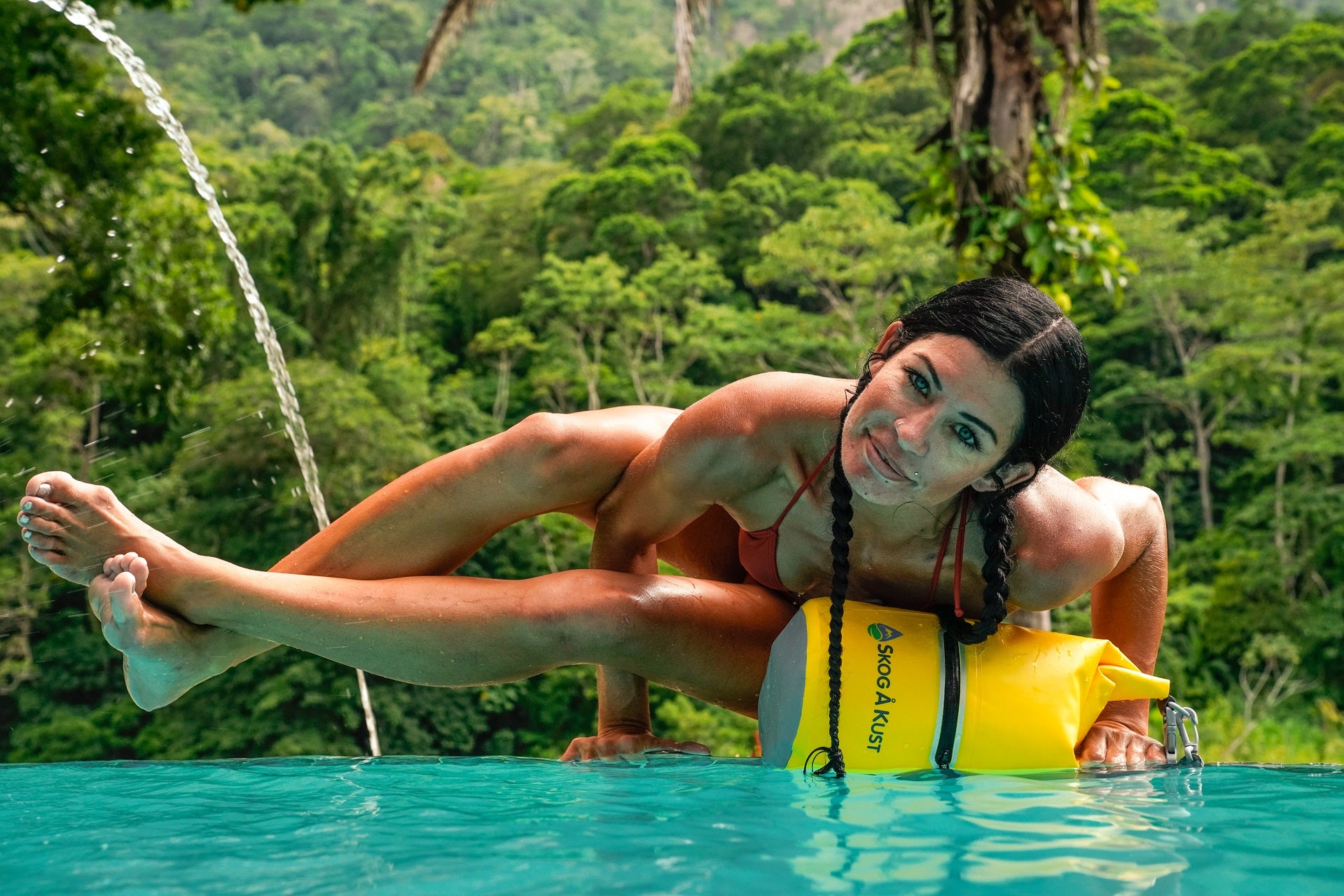The Skog A Kust yellow 10L DrySak waterproof dry bag being used to protect personal gear while exercising in the water with a jungle background