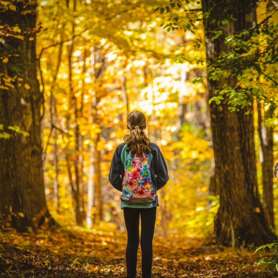 The Skog A Kust tie dye GymSak backpack with an internal dry bag is being worn by a girl walking through a forest in autumn